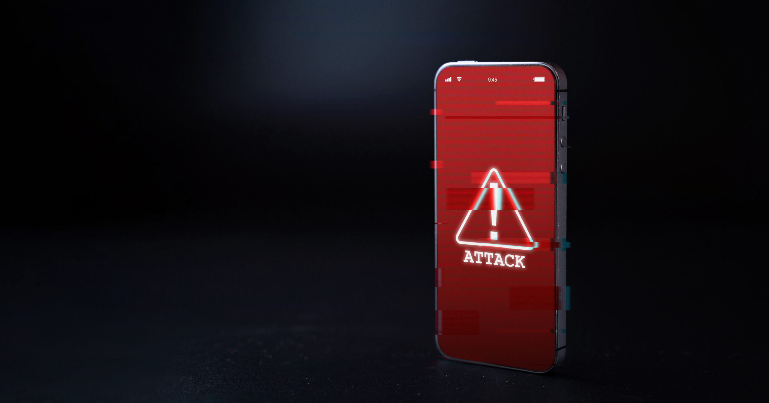 A smartphone with a glitching red screen. On the screen is a triangular caution sign and the word "ATTACK."