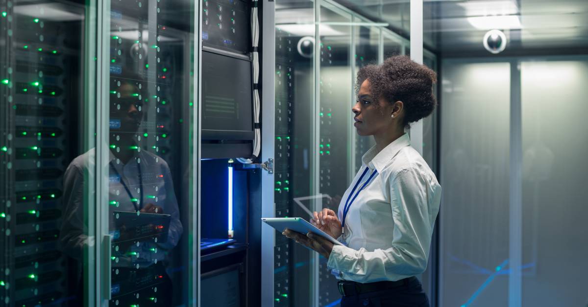 An employee in a data center holds a tablet and inspects a monitor attached to a multiple servers.