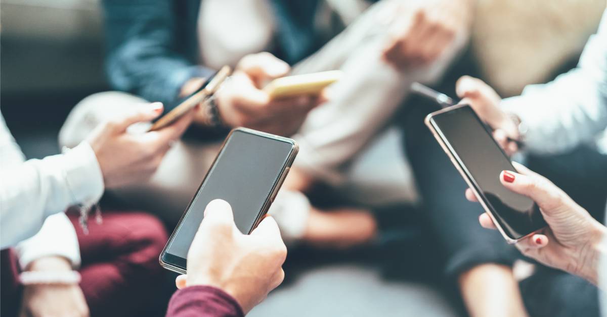 Five people in formal clothing sitting in a circle. All have their cell phones out to browse something.