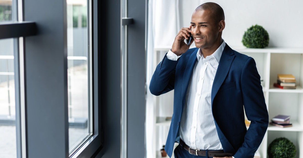 A man is wearing professional attire while looking out a nearby window and talking on a cell phone.