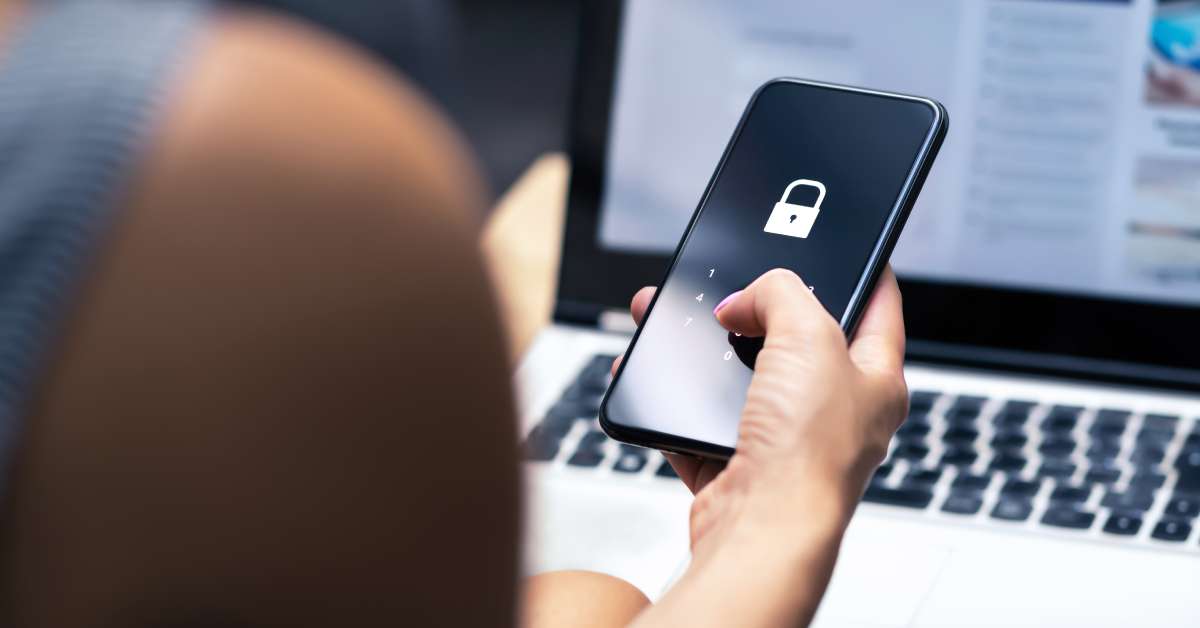 A person is using their thumb to type a security passcode on their cell phone under an image of a lock.