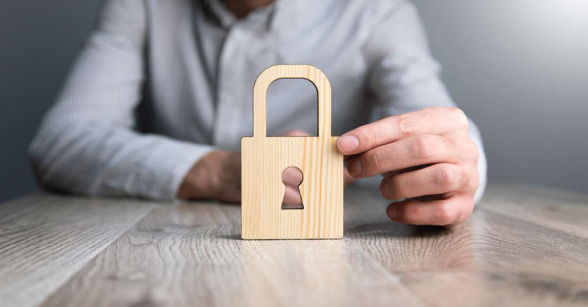 A wooden lock is on a grey wood table and someone is sitting behind the lock and touching it with their finger.