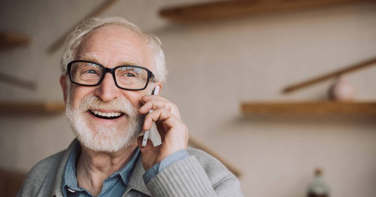 A person wearing thick black glasses is laughing while talking on their cell phone in front of wooden shelves.