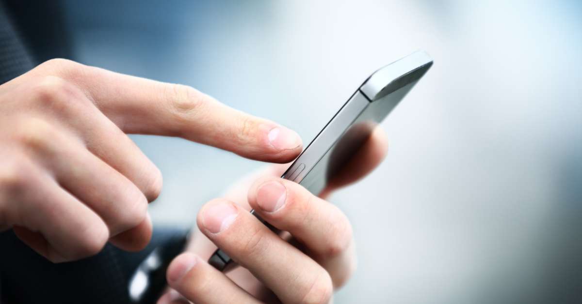 A person is using one hand to hold a small cell phone and the other hand to tap on its screen gently.