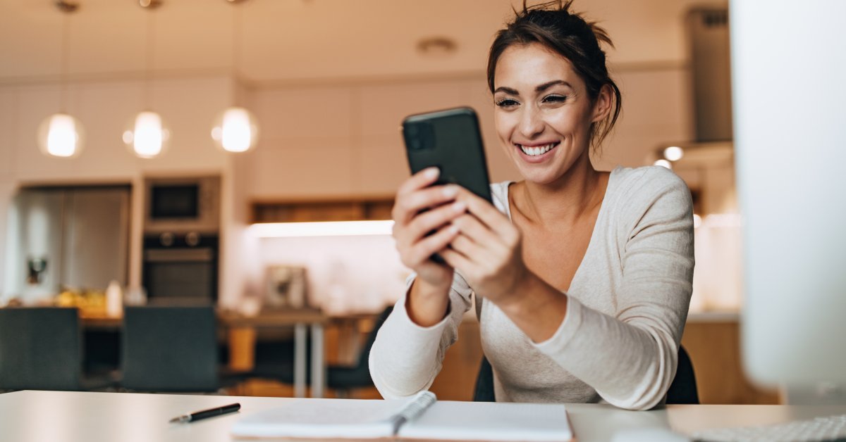 Someone is sitting down in a bright and clean kitchen while smiling and looking at their cell phone.