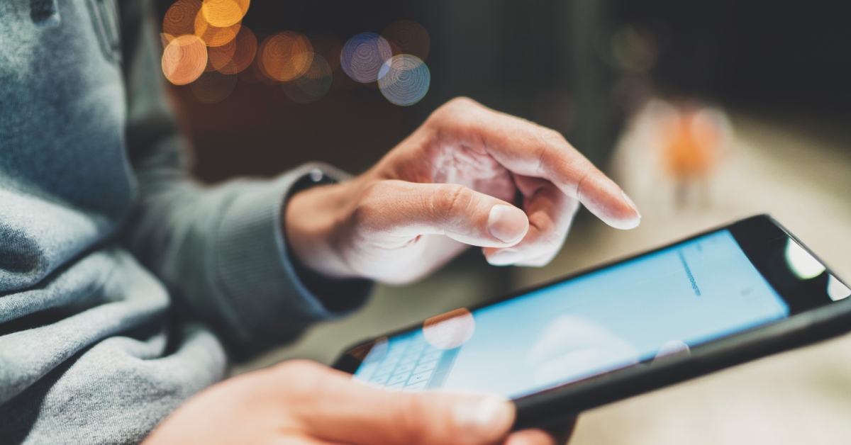 A person wearing a gray shirt is holding a tablet in front of them and using their finger to type on it.