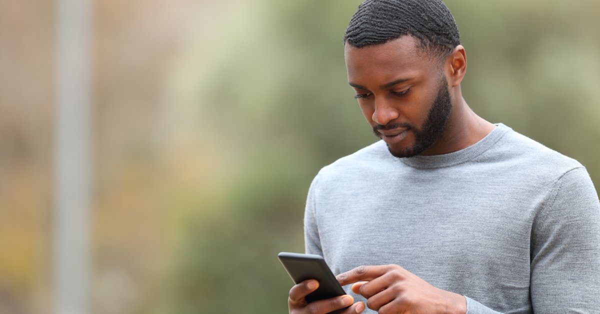 Someone using their cell phone while wearing a gray long-sleeve shirt and standing outside during the day.