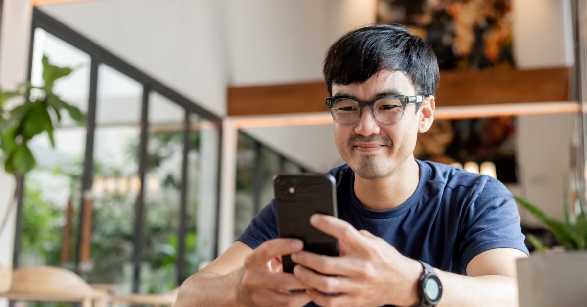 A person wearing a watch and glasses is using their cell phone. A painting hangs on the wall behind them.