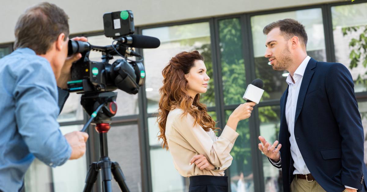 A cameraman is recording an interview between a journalist holding a microphone and someone wearing a suit.