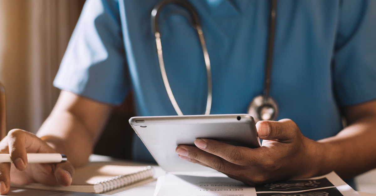 A healthcare professional wearing a blue medical uniform is holding a tablet in one hand and a pen in the other.