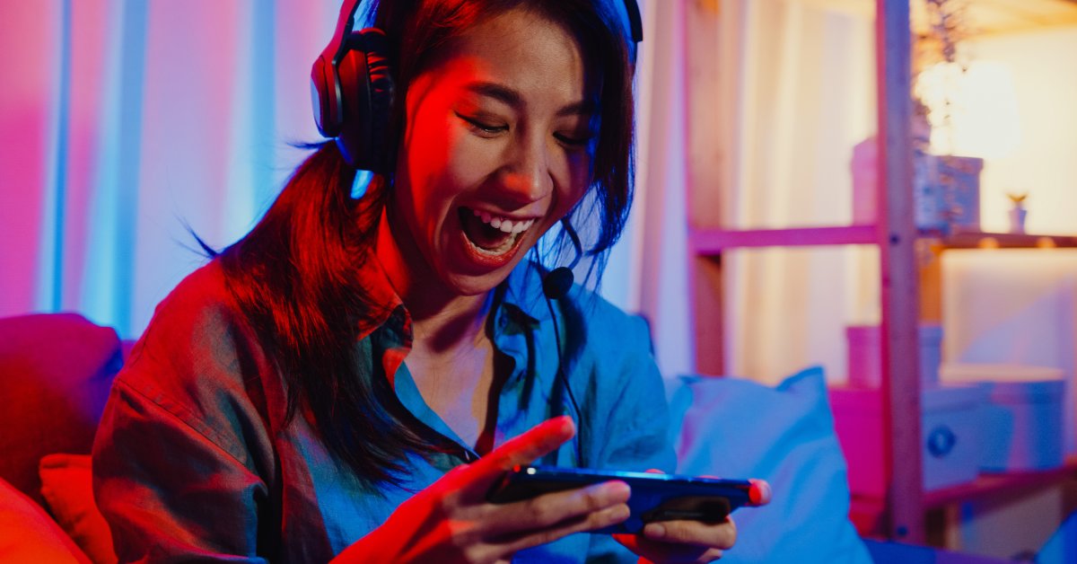 A person yells with excitement while playing a game on their phone. They are wearing headphones with a mic attached.