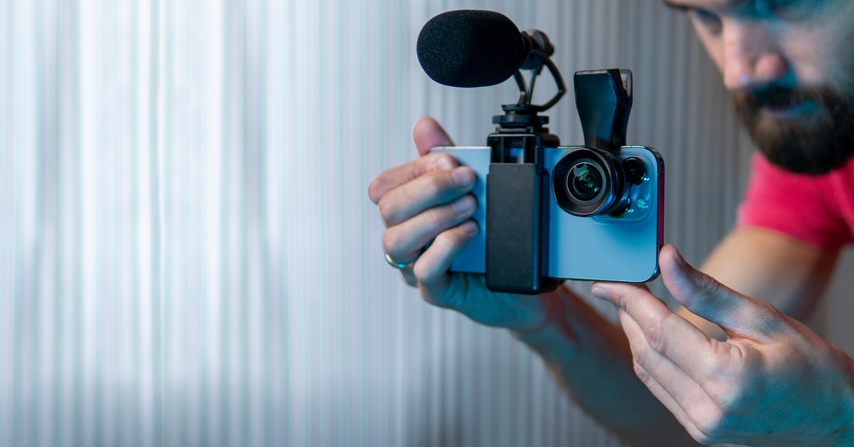 A director wearing a red shirt holds a cell phone with microphone and camera accessories attached to it.