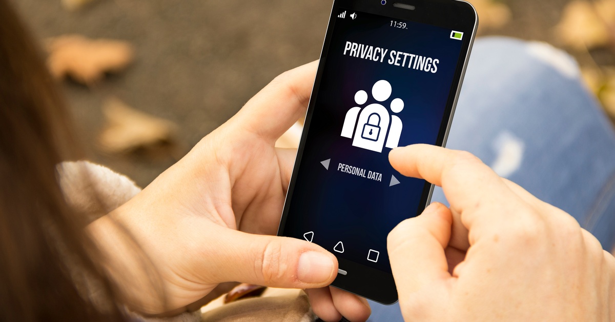 A person holds a cell phone in their hands. The phone screen reads “Privacy Settings” and “Personal Data.”